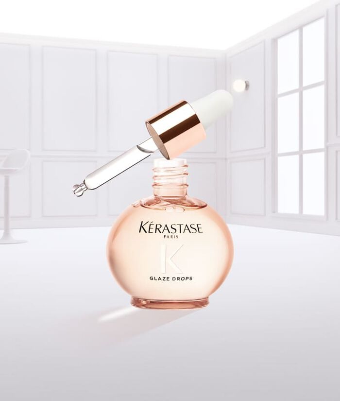 Frasco de suero Glaze Drops de Kerastase, con un liquido rosa goteando.