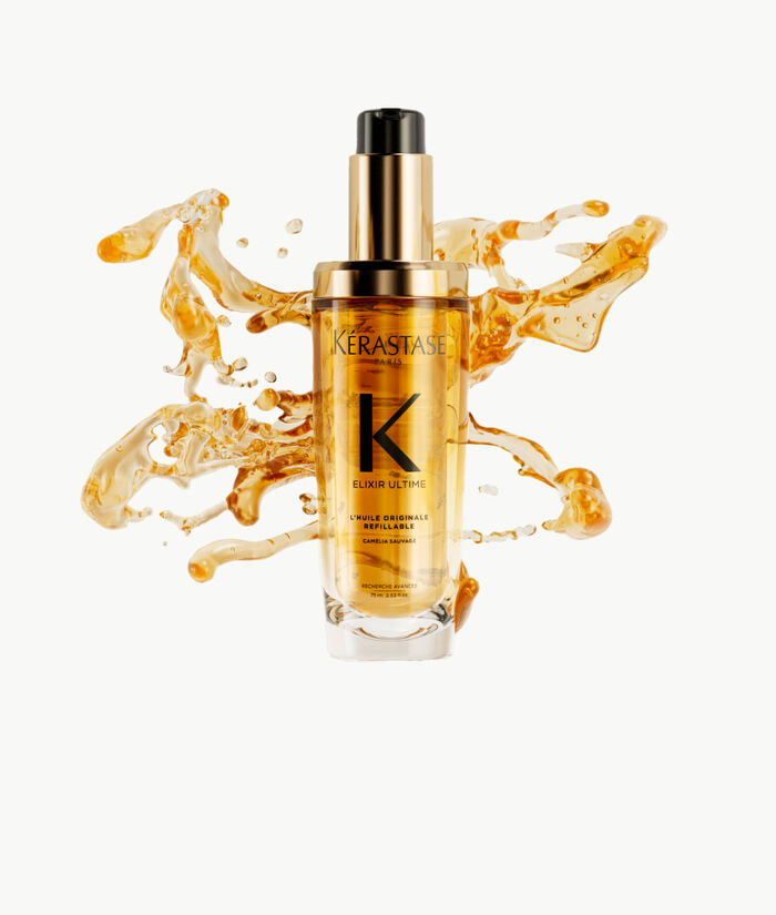 Frasco de suero Kerastase Elixir Ultime rodeado de gotas de aceite dorado sobre un fondo claro.