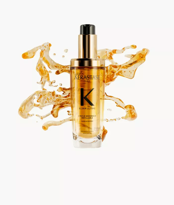 Frasco de suero Kerastase Elixir Ultime rodeado de gotas de aceite dorado sobre un fondo claro.