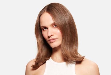 Retrato de una mujer con cabello castano de longitud media, brillante y bien peinado, sobre un fondo blanco.