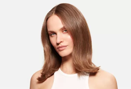 Retrato de una mujer con cabello castano de longitud media, brillante y bien peinado, sobre un fondo blanco.