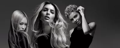 Three women with varying hairstyles pose against a dark background, showcasing stylish black outfits. Their expressions and hair create a dynamic, artistic composition.