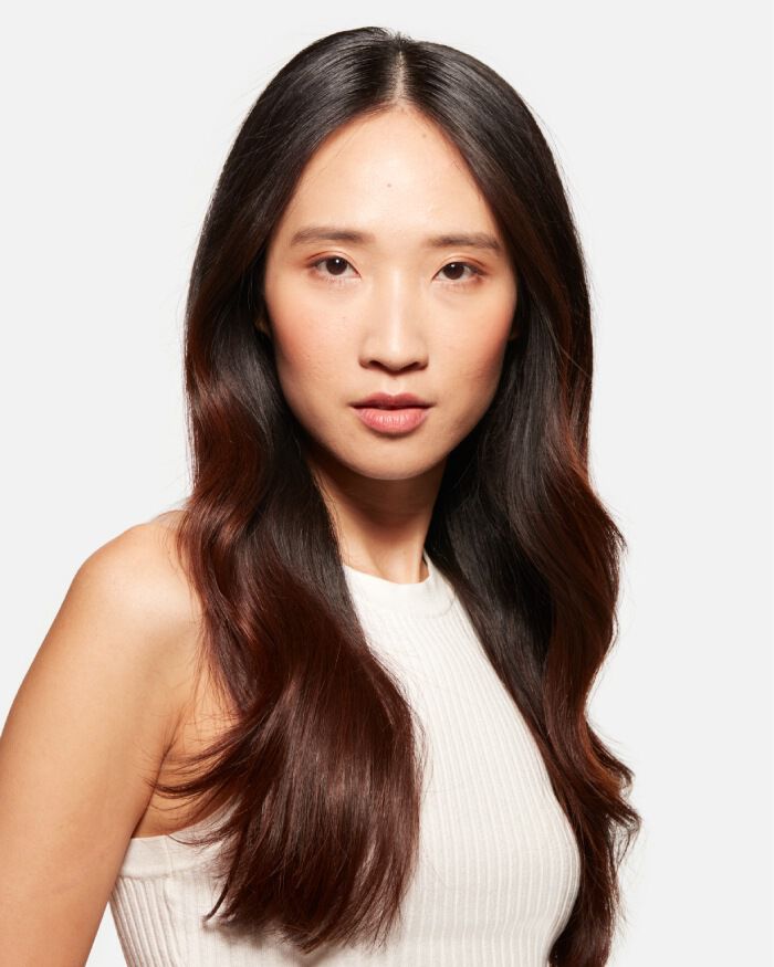 Retrato de una mujer con cabello largo y ondulado, con un fondo blanco, que mira directamente a la camara.