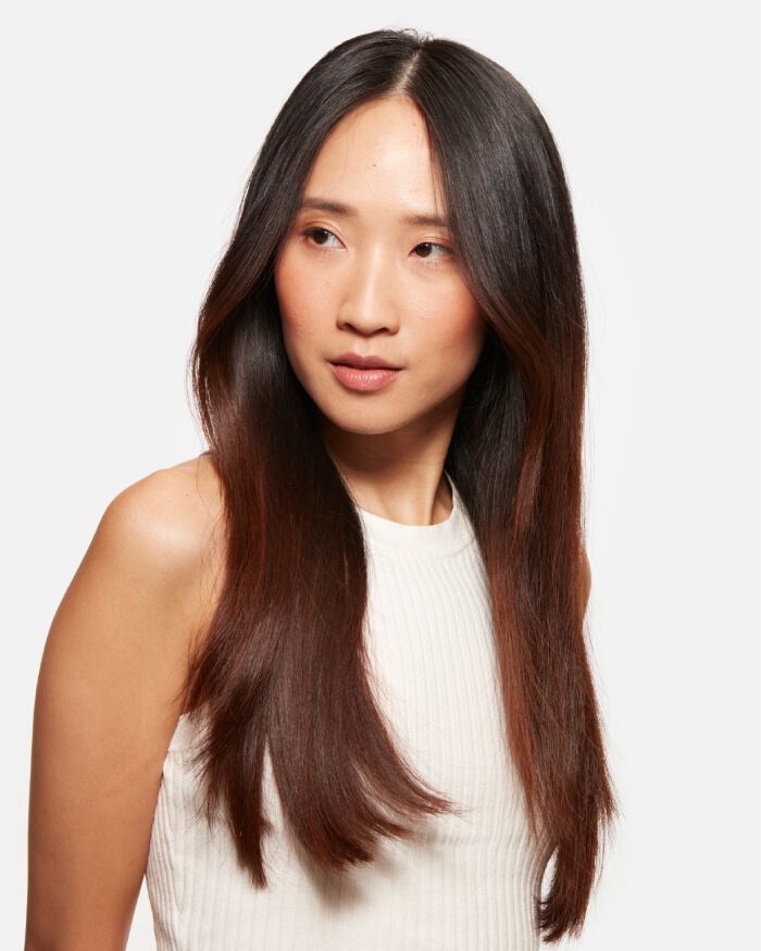 Mujer con cabello lacio y brillante, vestido blanco, mirando hacia un lado.