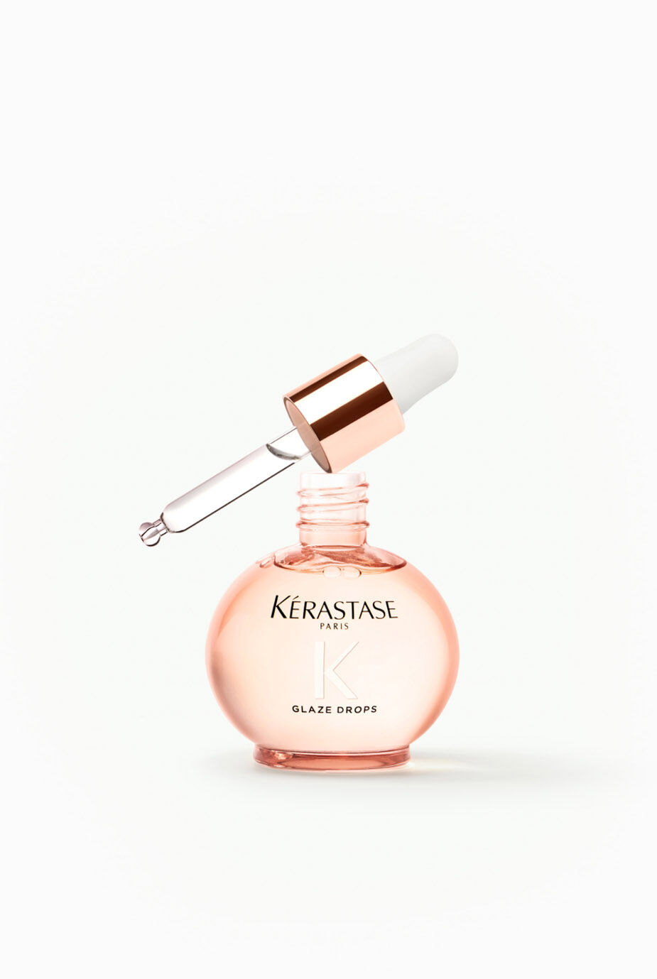 A round pink glass bottle of Kerastase Glaze Drops with a dropper lid, displayed against a light background.