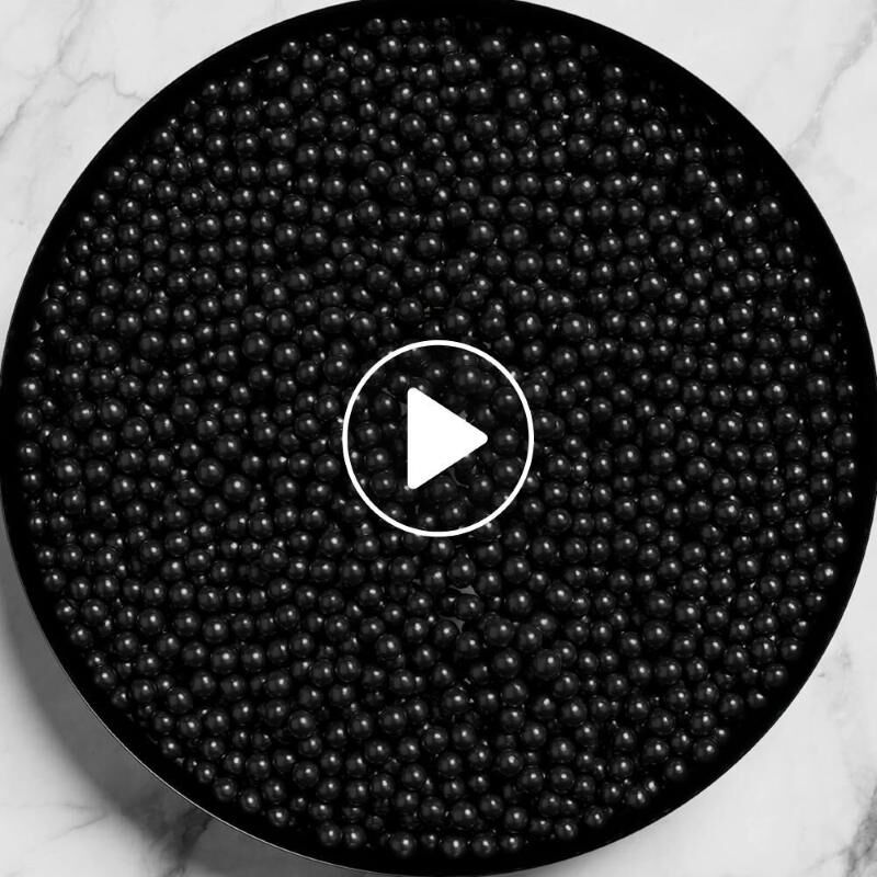 Una vista cenital de un recipiente circular lleno de muchas perlas negras pequenas y brillantes sobre una superficie de marmol.