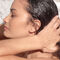 A profile view of a woman in the shower, with water running down her wet hair as she gently runs her fingers through it. The background features marble tiles.