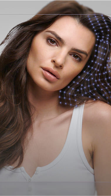 Una mujer con cabello castano oscuro y ondulado, luciendo una camiseta blanca, mira a la camara con una expresion serena. Un diseno de puntos azules se superpone a su cabello.