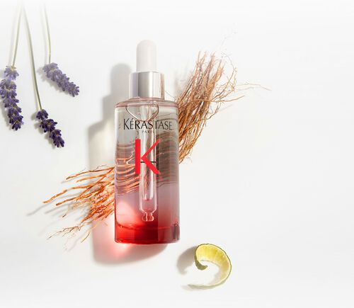Botella del serum Kerastase Genesis Serum Anti-Chute Fortifiant, rodeada de elementos botanicos como lavanda y jengibre.
