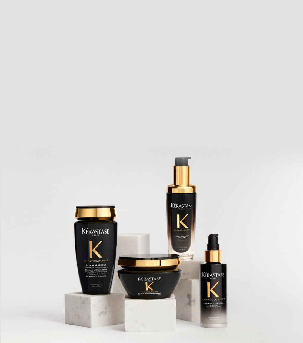 Productos capilares de la gama Kerastase Chronologiste en envases negros y dorados, dispuestos con elegancia sobre pedestales de marmol blanco ante un fondo claro.