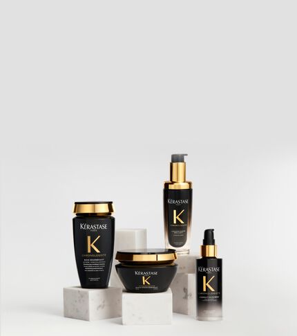 Productos capilares de la gama Kerastase Chronologiste en envases negros y dorados, dispuestos con elegancia sobre pedestales de marmol blanco ante un fondo claro.
