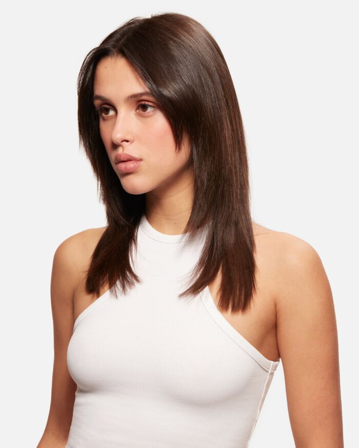 Mujer joven con cabello lacio y oscuro, mirando hacia un lado, vestida con una blusa sin mangas blanca.