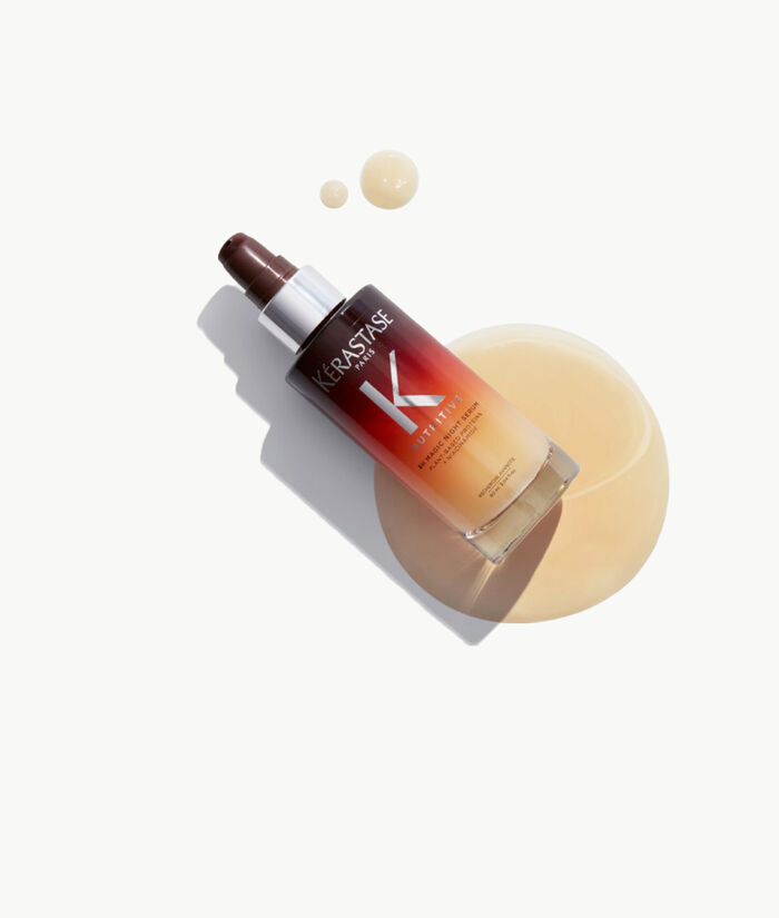 Botella de serum para el cabello de la marca Kerastase, con un liquido dorado derramado sobre la superficie.
