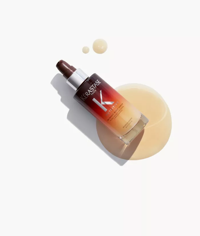Botella de serum para el cabello de la marca Kerastase, con un liquido dorado derramado sobre la superficie.