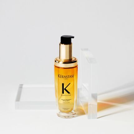 Botella de aceite de tratamiento para el cabello de Kerastase, con un envase dorado y transparente, sobre un fondo blanco.