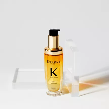 Botella de aceite de tratamiento para el cabello de Kerastase, con un envase dorado y transparente, sobre un fondo blanco.