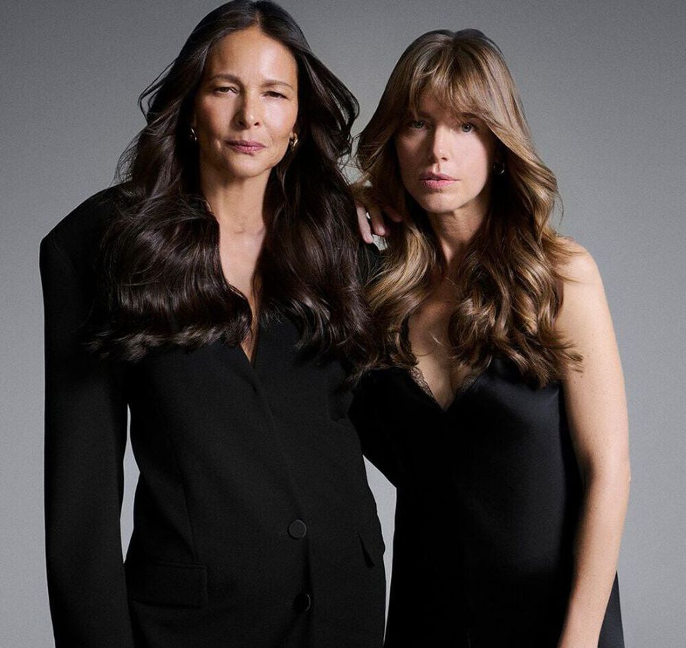 Dos mujeres posando juntas con elegantes atuendos negros, luciendo sus melenas largas y saludables.