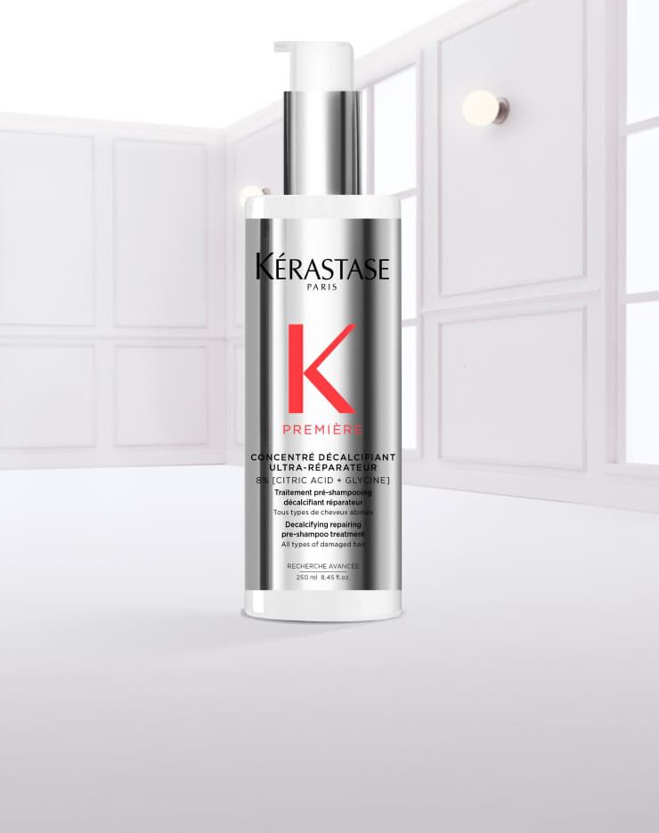 Botella de serum capilar de Kerastase, con liquido goteando y fondo claro.