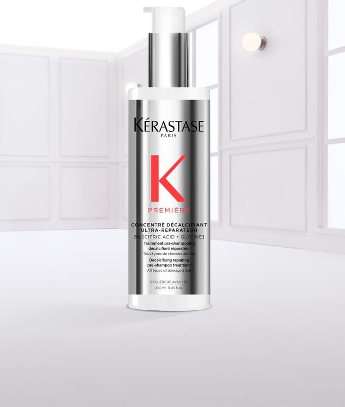 Botella de serum capilar de Kerastase, con liquido goteando y fondo claro.