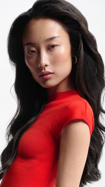 Mujer de cabello largo y oscuro moviendo su melena, vestida con top rojo, ilustrando el tratamiento adecuado contra la caida del cabello