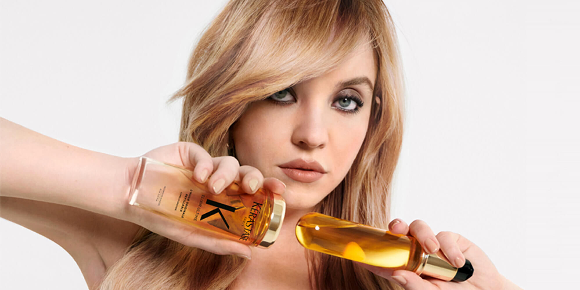 Una modelo sostiene dos botellas de producto para el cabello, con una expresion elegante.
