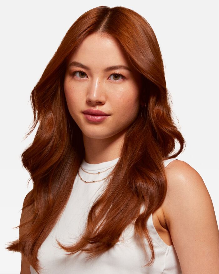 Retrato de una mujer con cabello largo y ondulado color castano claro, que lleva una blusa blanca y joyas delicadas.