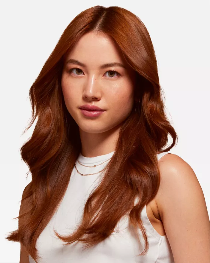 Retrato de una mujer con cabello largo y ondulado color castano claro, que lleva una blusa blanca y joyas delicadas.