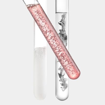 Un tubo de ensayo con liquido burbujeante de color rosa, colocado junto a un cilindro de muestra con liquido transparente.