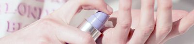Close-up image of a hand pressing a pump bottle to dispense a creamy product.