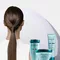Mujer con coleta brillante y productos Kerastase Resistance turquesa.