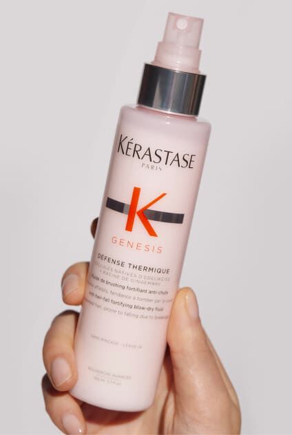 Mano sosteniendo una botella rosa de Kerastase Genesis Defense Thermique, un protector termico capilar.