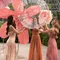 Three women in a botanical setting are joyfully interacting with a large, transparent orb surrounded by vibrant flower decorations.
