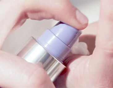 Close-up image of a hand pressing a pump bottle to dispense a creamy product.