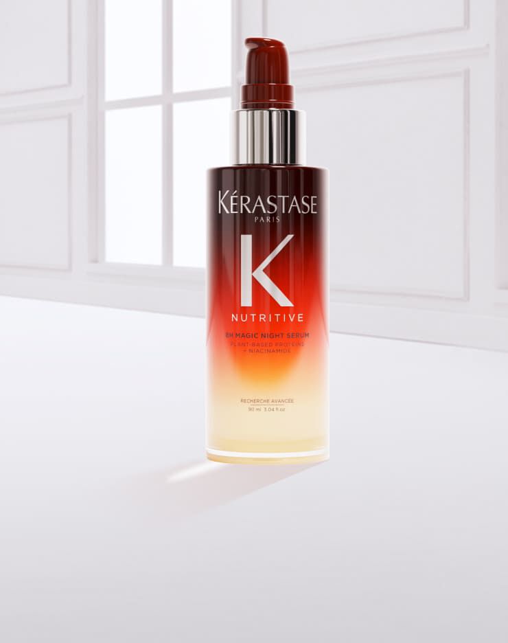 Botella de serum para el cabello de la marca Kerastase, con un liquido dorado derramado sobre la superficie.