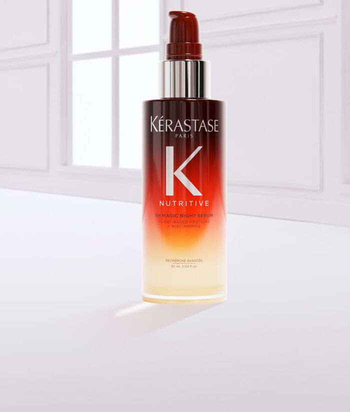Botella de serum para el cabello de la marca Kerastase, con un liquido dorado derramado sobre la superficie.