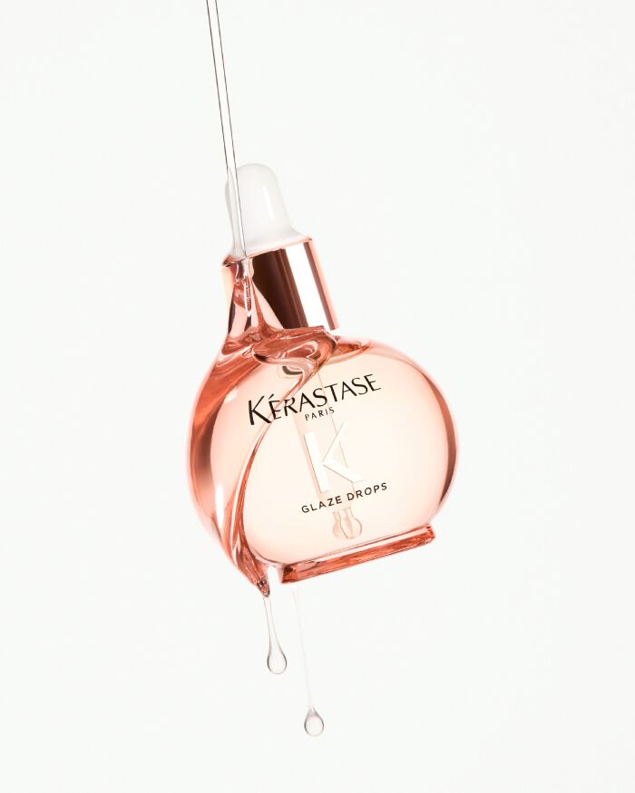 Frasco de suero Glaze Drops de Kerastase, con un liquido rosa goteando.