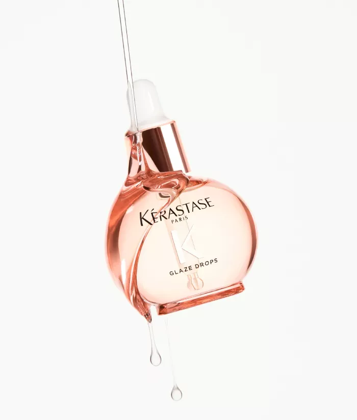 Frasco de suero Glaze Drops de Kerastase, con un liquido rosa goteando.