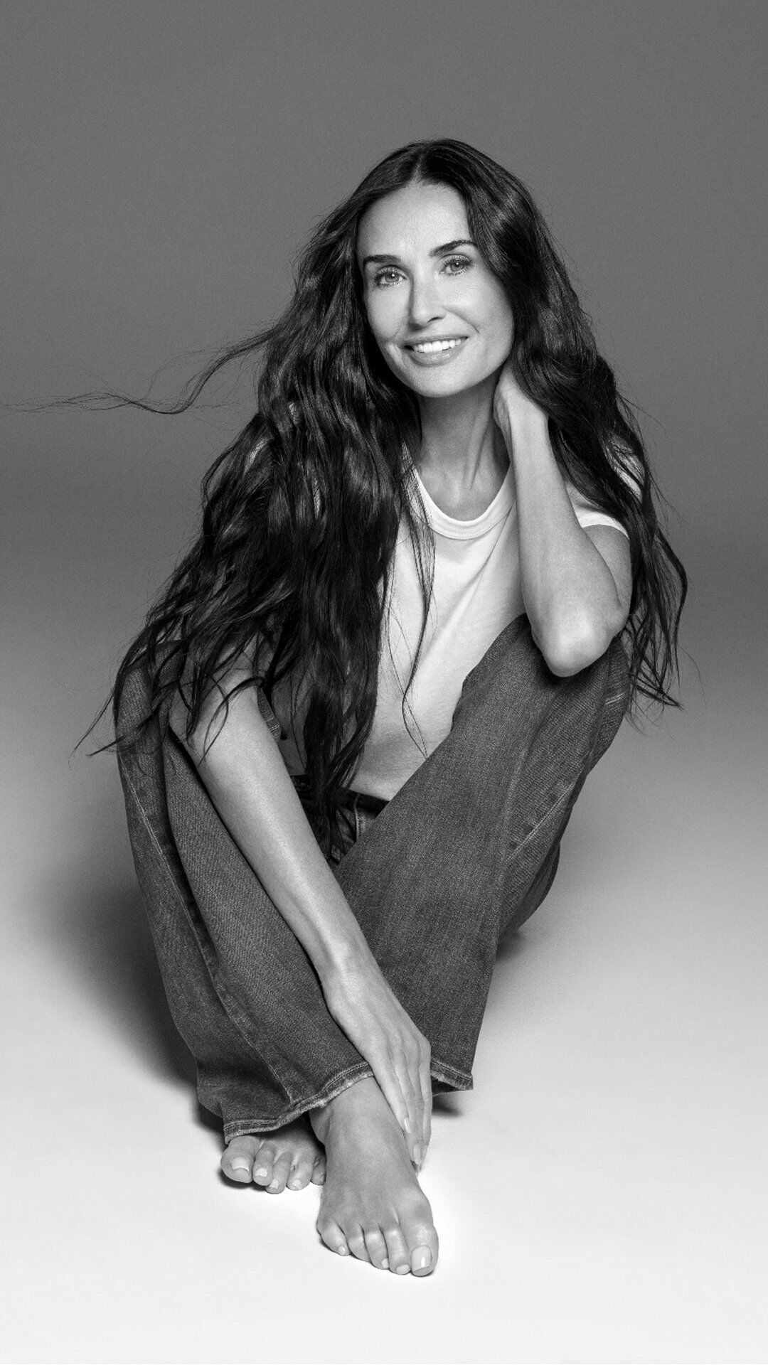Demi Moore sentada con las piernas cruzadas y una gran sonrisa radiante.