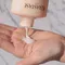 A person's hand holding a bottle of Kerastase hair product, with a small amount of creamy lotion being poured into the palm. The background features a marble surface.