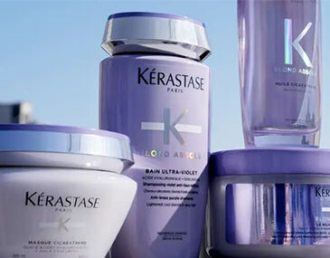 Four Kerastase hair care products in purple containers are displayed against a bright background, featuring labels with the brand name and product details.