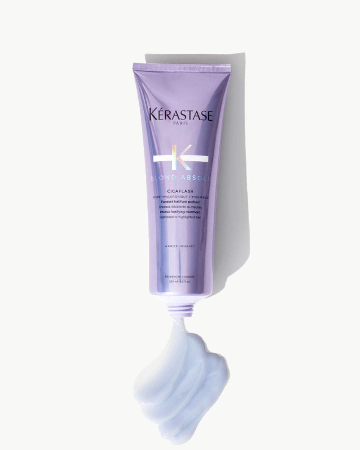 Imagen de un tubo de tratamiento para el cabello de Kerastase, llamado "Cicaflash", con un diseno en tonos morados y un poco de producto en una textura cremosa en la parte inferior.