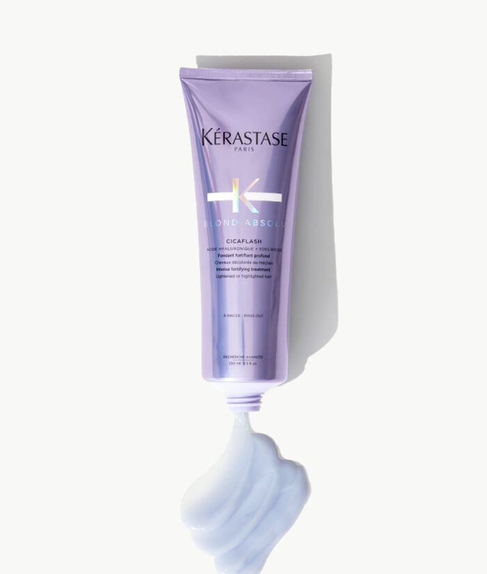 Imagen de un tubo de tratamiento para el cabello de Kerastase, llamado "Cicaflash", con un diseno en tonos morados y un poco de producto en una textura cremosa en la parte inferior.