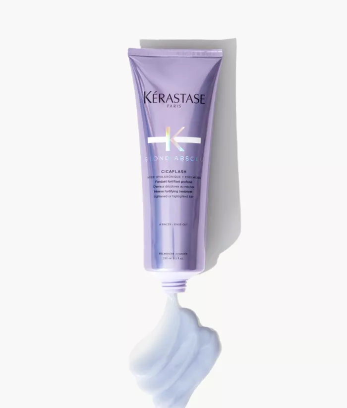 Imagen de un tubo de tratamiento para el cabello de Kerastase, llamado "Cicaflash", con un diseno en tonos morados y un poco de producto en una textura cremosa en la parte inferior.