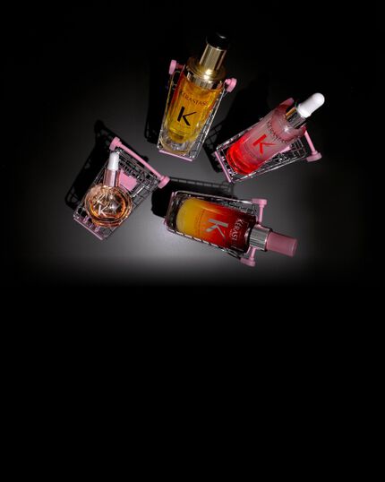 Cuatro productos capilares Kerastase en mini-carritos rosas sobre fondo negro: el Serum Noche 8H Nutritive, el Aceite Original Elixir Ultime, el Serum Anticaida Fortificante de Genesis y las Glaze Drops.