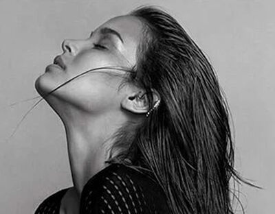 A close-up of a woman with long, wet hair cascading down her back, her head tilted slightly back, and her profile elegantly highlighted against a neutral background.