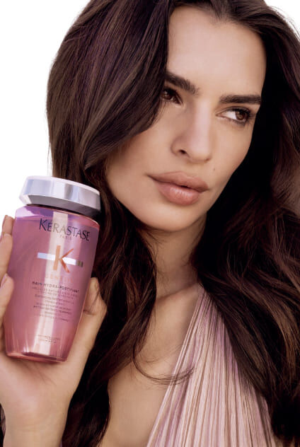 Mujer sosteniendo una botella de champu Kerastase Genesis Bain Hydra-Fortifiant, destacando el producto.