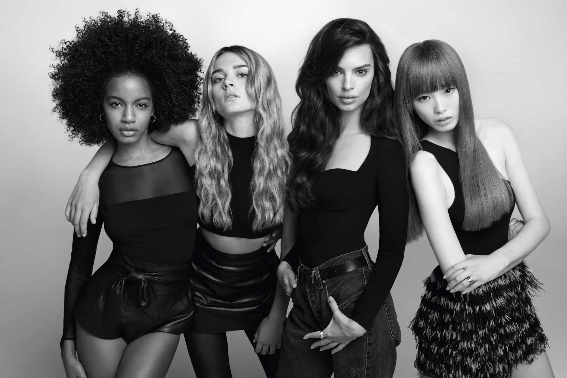 A group of four diverse women poses together in a stylish black and white photograph. They have various hairstyles and outfits, exuding confidence and elegance.