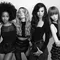 A group of four diverse women poses together in a stylish black and white photograph. They have various hairstyles and outfits, exuding confidence and elegance.