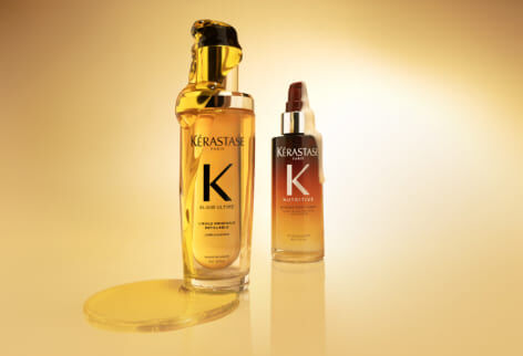 Dos productos Kerastase, el Aceite Original Elixir Ultime (frasco dorado) y el Serum Noche 8H Nutritive (frasco degradado naranja), sobre un fondo amarillo dorado.