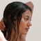 A profile view of a woman with long, wet hair, gently combing her hair while her hand is positioned behind her head. The background is neutral and minimalistic.
